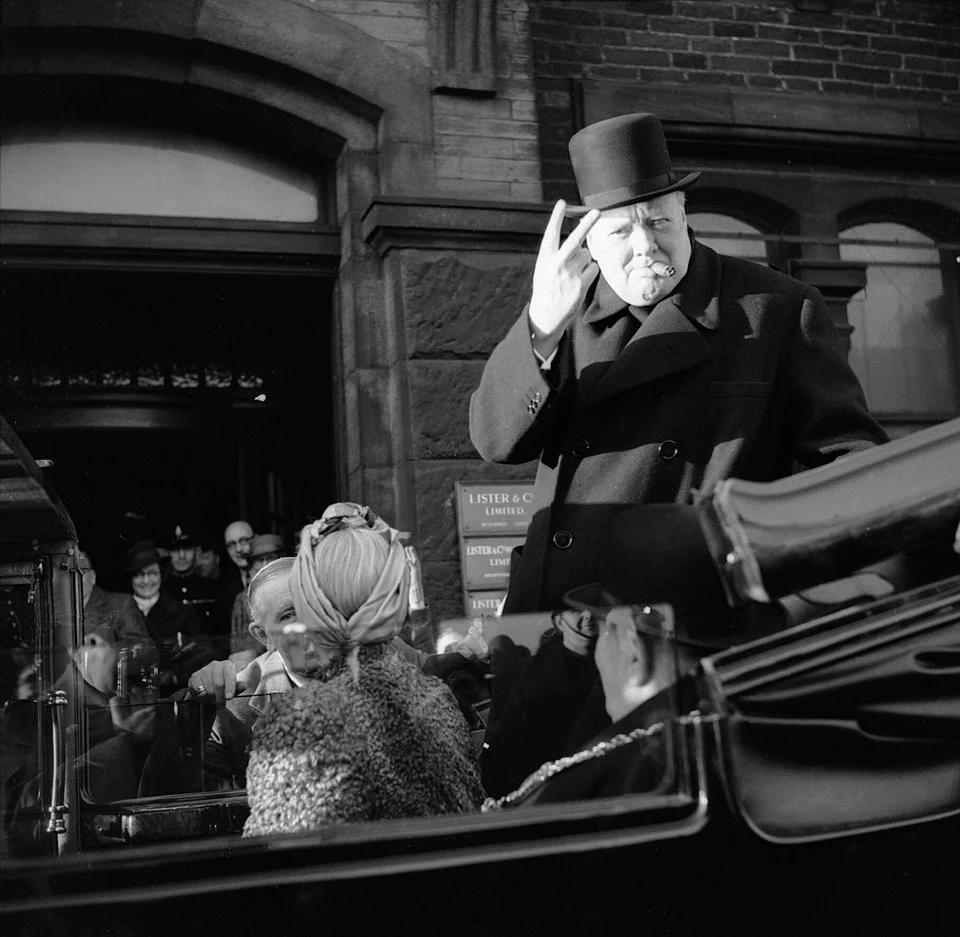 A photo of Winston Churchill in 1942, riding in a car, directing an outward two-fingered salute (with palm facing towards him) to the camera. Photo is taken from Wikipedia's page named "V sign".
