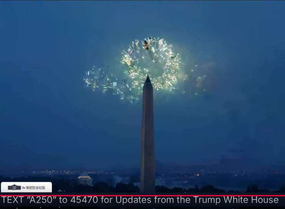 A screenshot of the whitehouse live stream of the parade. The washington monument at dusk with white fireworks ejaculating behind the tip of the monument