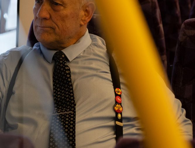 Cropped photo of Williams on a vline train with badges on his suspenders supporting Aboriginal rights, Yes for that referendum, and anti-nuclear