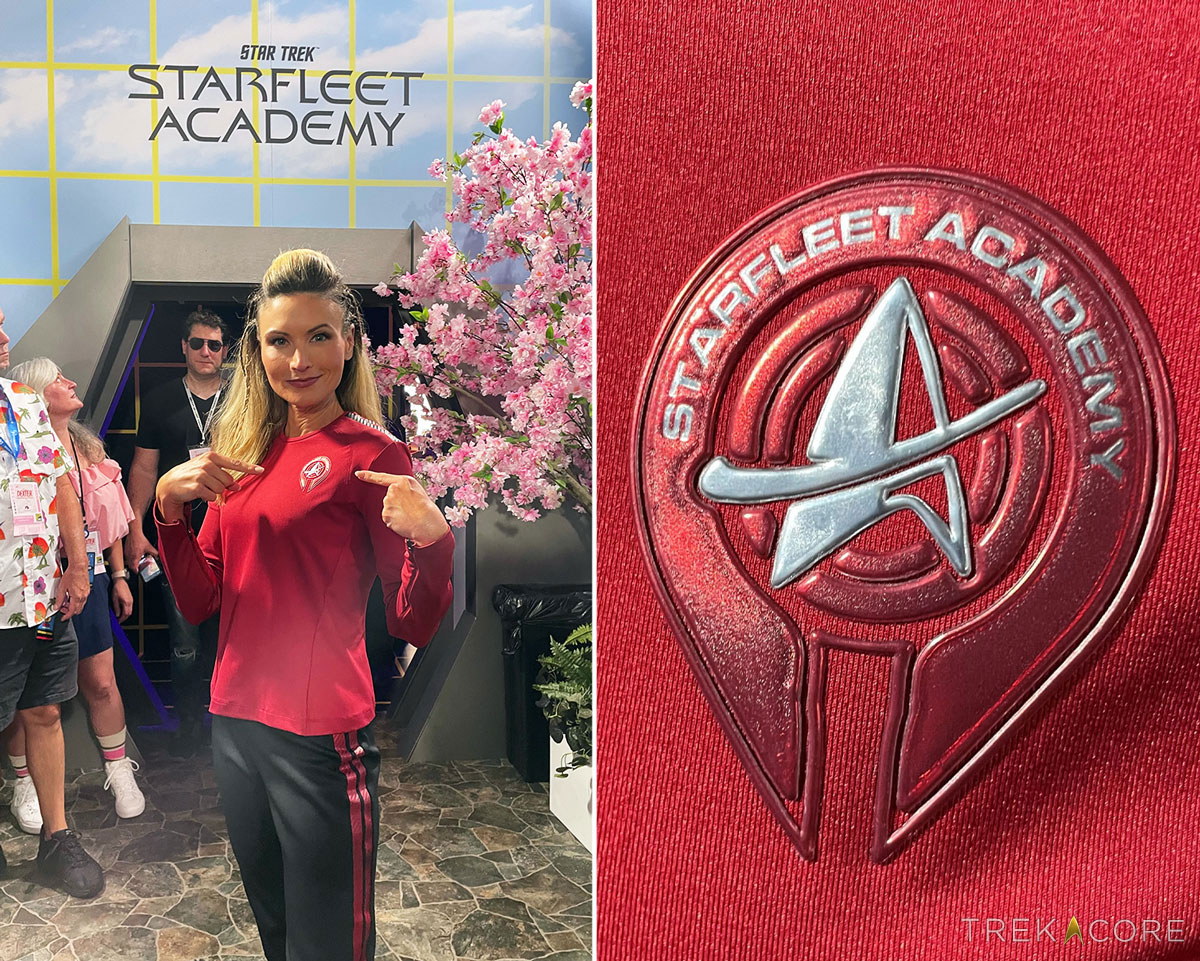 A blonde, female model at San Diego Comic-Con. She is wearing a red tunic with black striping along the top of the shoulders. On her chest is a Starfleet Academy symbol, featuring a Discovery-style split delta with a "swoosh" around it, surrounded by two broken concentric circles, which are futher surrounded by a U-shape that is open at the bottom. Her pants are black, with two red stripes running down the side of her leg.